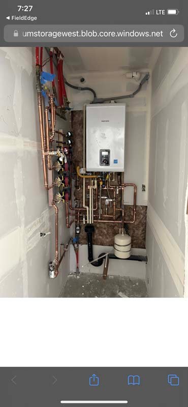 Narrow utility room with intricate piping and water heater