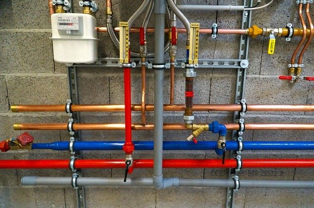 Color-coded plumbing pipes and meters on grey wall