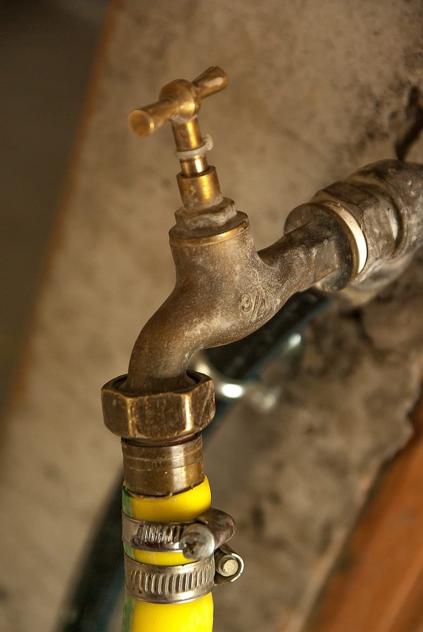 Old brass faucet connected to yellow hose