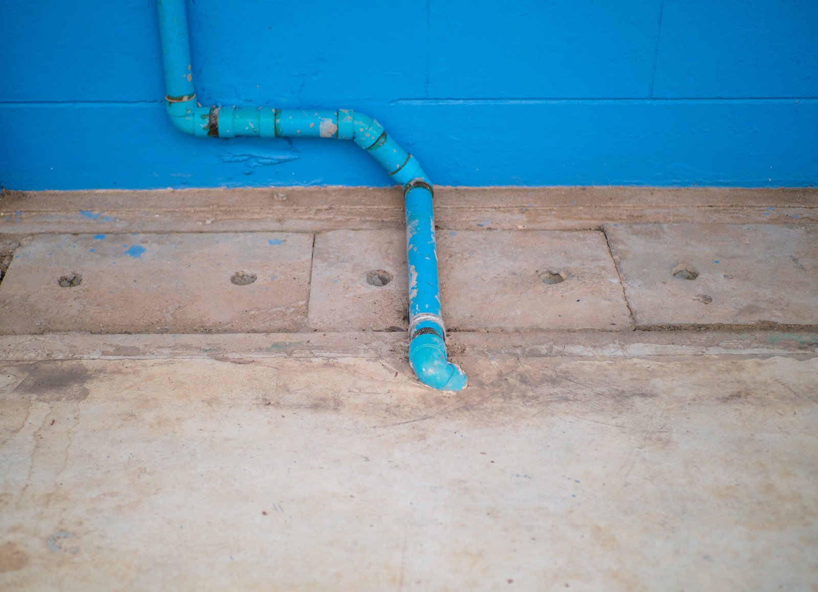 Worn teal pipe against vibrant blue wall